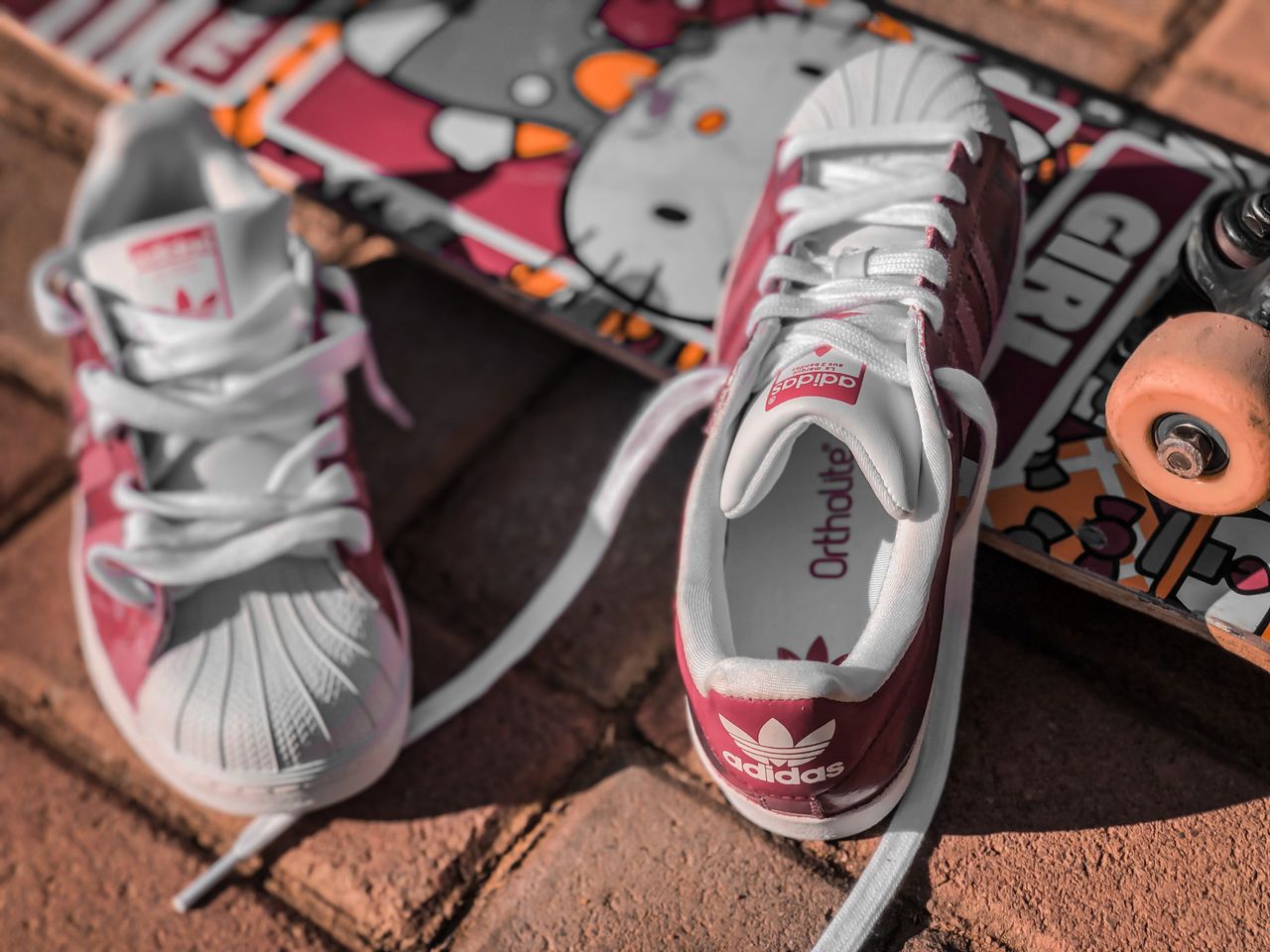 Close-up of Adidas sneakers and colorful skateboard on outdoor pavement, showcasing urban style.